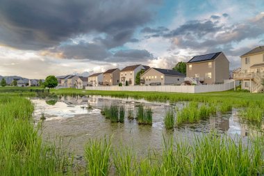 Çok katlı evleri ve parlak göleti olan manzaralı bir mahallede bulutlu bir gökyüzü.