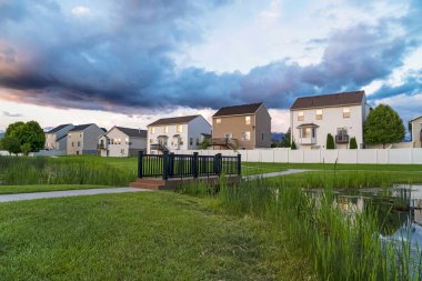 Köprüsü olan gölet, balkonlu ve pencereli evlerin önündeki parkta.