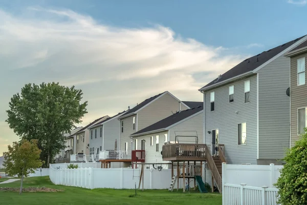 Çimenli bahçeli evler, balkonlar, merdivenler ve beyaz çitler.