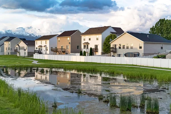 Casas y cielo nublado reflejado en la superficie brillante de un estanque cubierto de hierba — Foto de Stock