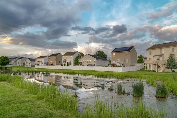 Bulutlu gökyüzünün altındaki manzaralı bir mahallede, evlerin önündeki bir parkta gölet.