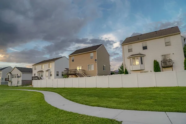 Evlerin ön cephesi ve gökyüzünün altındaki çimenler gri bulutlarla kaplı.