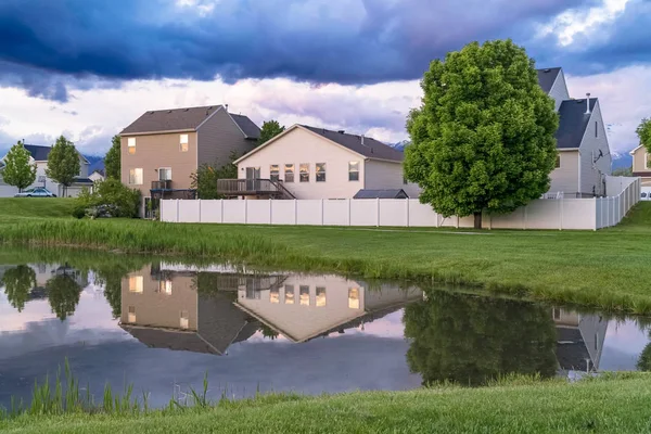 Houses trees and cloudy sky reflected on the shiny surface of a pond — Stock Photo, Image