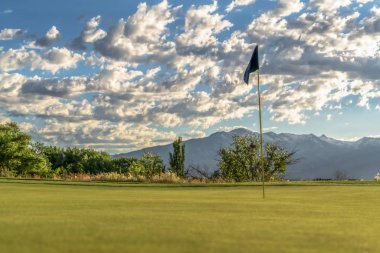 Ağaçlara ve bulutlu gökyüzüne karşı bir golf sahasının bayrak direğine odaklan