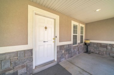 Beton ve taş duvarlı bir evin girişindeki beyaz kapı ve pencereler.