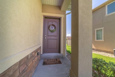 Bir evin ön cephesinde çelenkle süslenmiş küçük veranda ve kahverengi kapı.