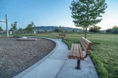 Uzak dağ manzaralı parktaki ahşap banklar ve gün batımında açık gökyüzü.