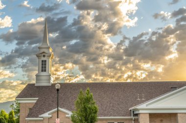 Çan kulesine sahip kilise, karanlık çatı ve bulutlu mavi gökyüzüne bakan tuğla duvar.