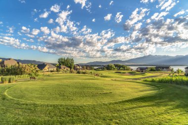 Evler göl ve dağ arka plan ile güneşli bir günde bir golf sahası görünümü