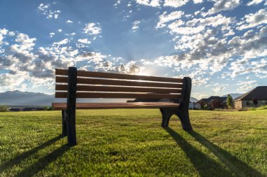 Parlak güneş ve bulutlu mavi gökyüzüne karşı bir açık park bankı arka görünümü