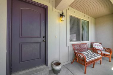 Verandada kahverengi ön kapı ve mobilya ile bir evin ön görünümü