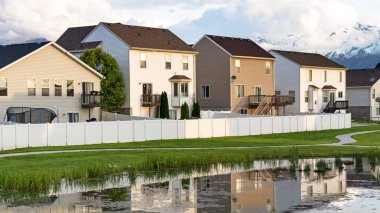 Panorama evleri ve bulutlu gökyüzü çimenli bir göletin parlak yüzeyine yansıyor.