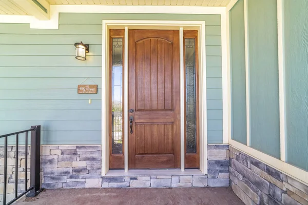 Front view of a home with green wall and brown wood door flanked by sidelights