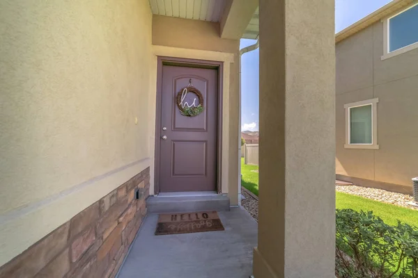 Bir evin ön cephesinde çelenkle süslenmiş küçük veranda ve kahverengi kapı.