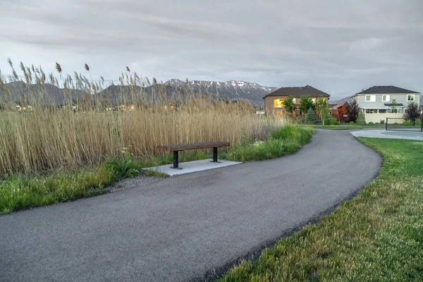 Straße mit Bank auf der Seite inmitten einer Rasenfläche und Häusern in der Ferne — Stockfoto