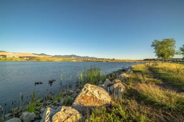 Lac pittoresque avec chemin de terre sur son rivage herbeux et rocheux vu sous le ciel bleu — Photo