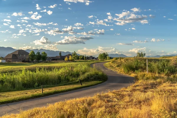 Terreno gramado com estrada sinuosa vista sob nuvens e céu azul em um dia ensolarado — Fotografia de Stock