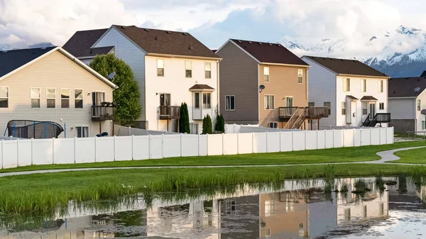 Panorama evleri ve bulutlu gökyüzü çimenli bir göletin parlak yüzeyine yansıyor.