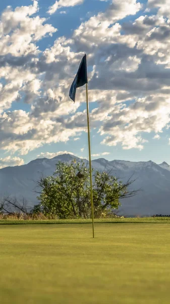 Vertikální rám Soustřeďte se na vlajku golfového hřiště proti stromům na horské a oblačné obloze — Stock fotografie