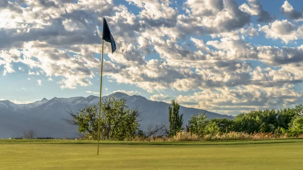 Panorama Soustřeďte se na vlajku golfového hřiště proti stromům na horské a oblačné obloze — Stock fotografie