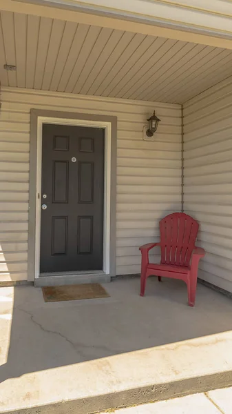 Poltrona de madeira vermelha vertical pela porta marrom no pequeno alpendre frontal de uma casa — Fotografia de Stock