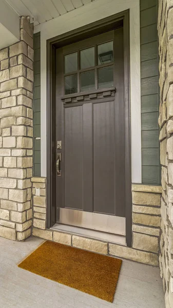 Vertical Home entrance with a glass paned brown wooden door and stone brick wall