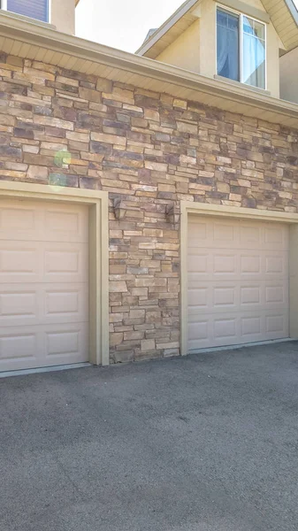 Vertical White garage doors of a home against exterior wall covered with stone bricks