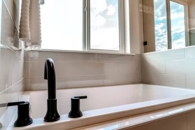 Banyoya döşenmiş siyah musluklu küvet fayans duvarı ve zemini var.