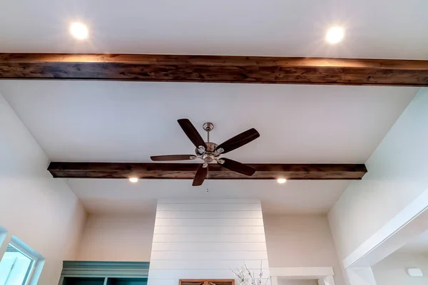 Ceiling fan with lights between decorative wood beams inside living room of home