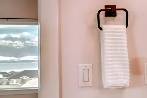 Vit handduk hängande på fyrkantiga handdukshållare bredvid elektrisk rocker strömbrytare — Stockfoto