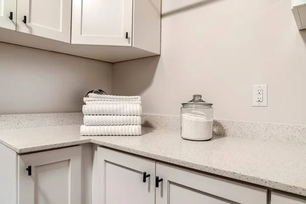 Countertop with jar of powder detergent and folded towels over wood cabinets