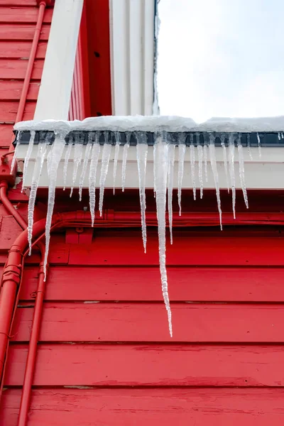 Spiked frozen icicles at the roof of home with vibrant red wooden exterior wall
