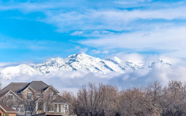 Picos de una magnífica montaña nevada sobre nubes bajas e hinchadas contra el cielo azul — Foto de Stock