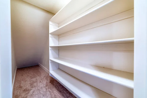 Small walk in closet with empty long cabinet shelves under slanted ceiling — Stock Image Small walk in closet with empty long cabinet shelves under slanted ceiling Stock Image