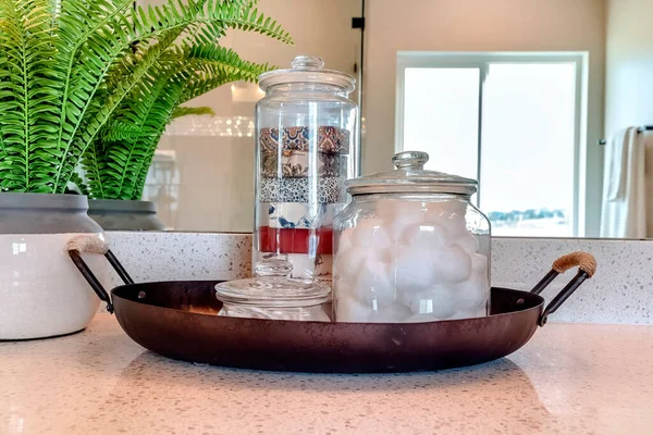 Jars of soap cotton balls and buds on metal tray beside potted leafy green plant