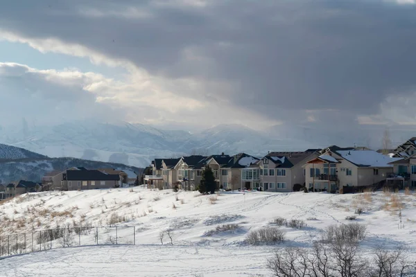Casas en terreno nevado ovelooking Wasatch Mountain pico y cielo nublado oscuro — Foto de Stock