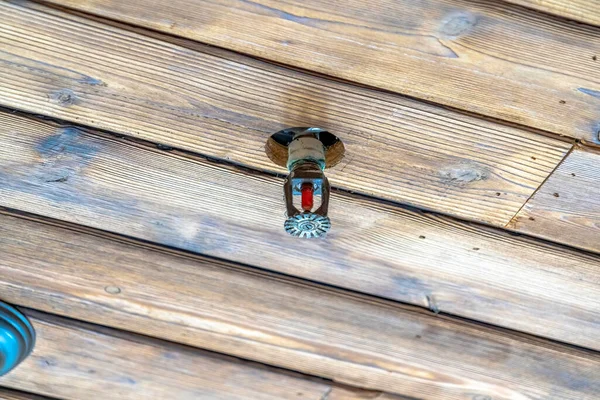 Fire sprinkler head installed on the brown wooden ceiling of a building or home