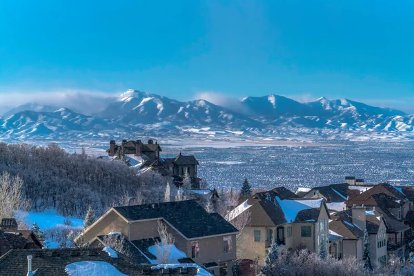 Snow falling on homes with sweeping view of valley and towering Wasatch Mountain