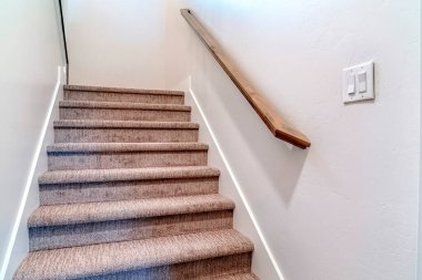 Evin içinde halı döşeli, beyaz duvarda kahverengi tırabzan var.