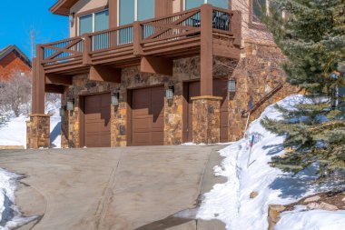 Güneşli bir kış gününde, karlı bir zeminin ortasında üç araba garajıyla ev cephesi