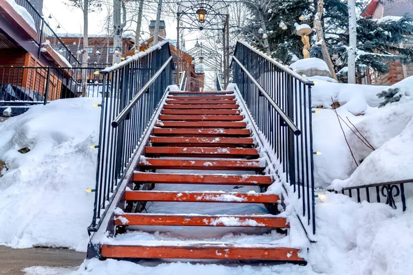 Escaleras contra la pendiente cubierta de nieve con casas y árboles bajo el cielo nublado de invierno — Foto de Stock