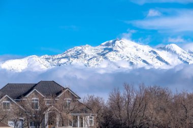 Güneşli karlı dağ alçak gri bulutların üzerinde canlı mavi gökyüzüne karşı