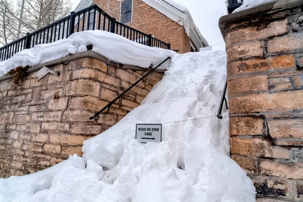 Snowed in stairs amid stone retaining wall with home and cloudy sky background