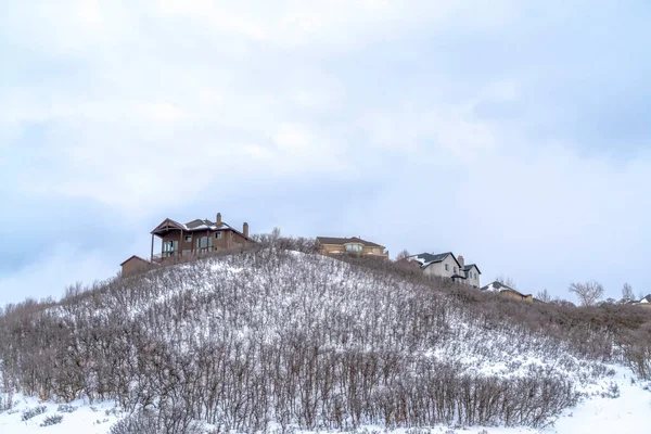 Huizen bovenop een heuvel met bladloze struiken op de helling bedekt met sneeuw in de winter — Stockfoto