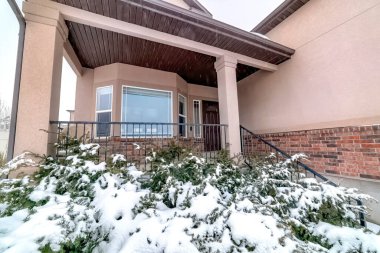 Tuğla evin bahçesinde, verandası ve penceresi olan karlı Evergreen 'ler.