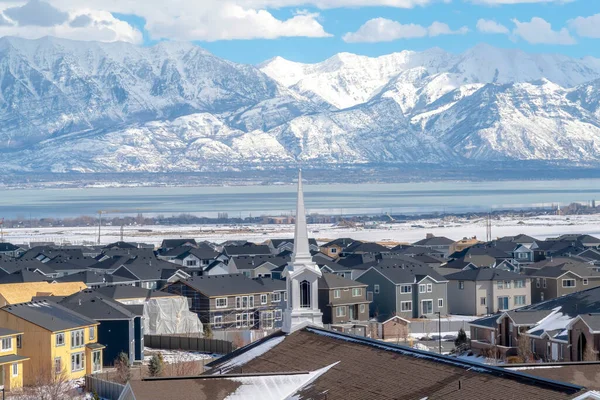 Church spire against neighborhood homes with snowy mountain and scenic lake view