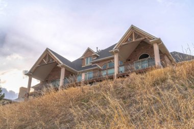 Yurt ve balkonun üstündeki bulutlu arka planda iki gable çatısı olan ev.