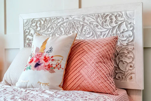 Fluffy pillows against decorative headboard of single bed against panelled wall