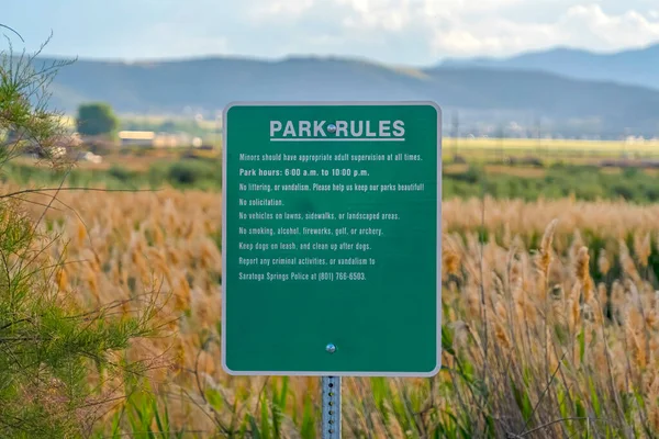 Tablero de letreros verde con reglas del parque contra exuberantes hierbas altas en un vasto terreno — Foto de Stock