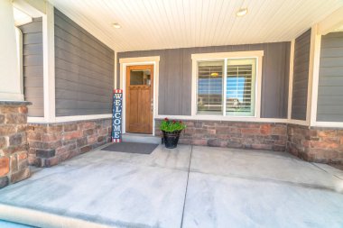 Beton verandalı ev girişi. Kahverengi ahşap ön kapı. Hoş geldin işareti.